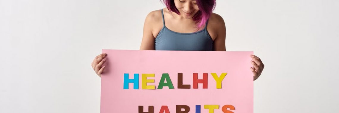 Asian woman holding a colorful 'Healthy Habits' sign in a studio setting, promoting wellness.
