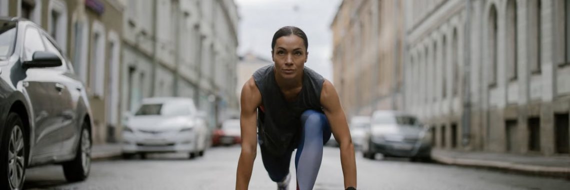Woman in activewear poised for a run on a city street, symbolizing fitness and determination.